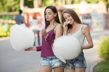 İki genç kadın pamuk candyfloss eğlence parkı paylaşımı. En yakın arkadaşlarım pamuk şeker birlikte açık havada yemek.