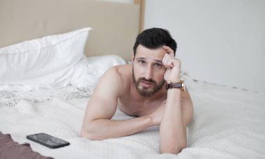 Mutlu rahat genç gülümseyen ve yatakta yatan adam. Seksi sakallı adam yatakta.