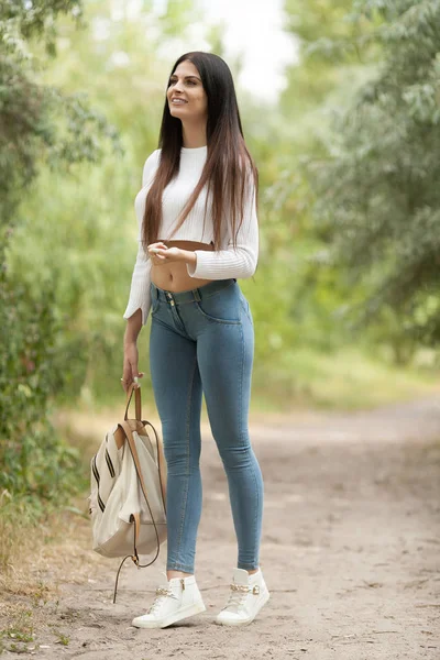 Sexy brunette woman in blue jeans with long hair walk with backpack. — Stock Photo, Image