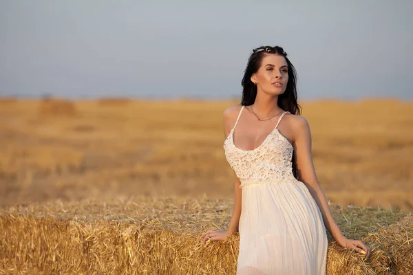 Atractiva mujer con estilo en vestido largo de verano blanco cerca de la paca de heno en el prado —  Fotos de Stock