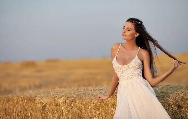 Atractiva mujer con estilo en vestido largo de verano blanco cerca de la paca de heno en el prado —  Fotos de Stock