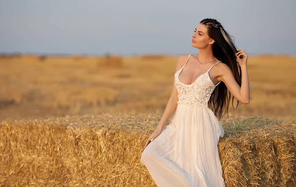 Atractiva mujer con estilo en vestido largo de verano blanco cerca de la paca de heno en el prado —  Fotos de Stock