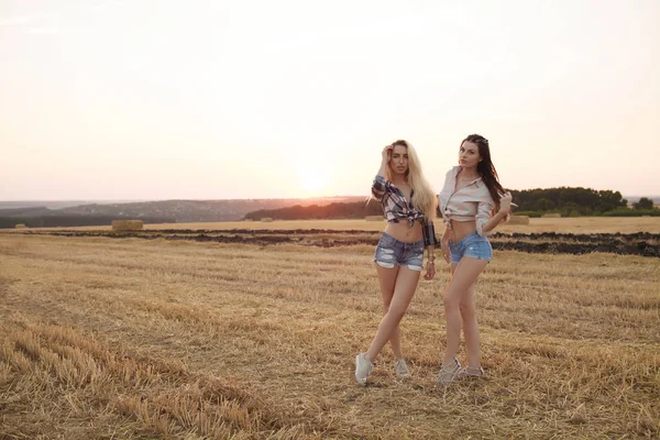 Dos novias van al atardecer. Sexy rubia y morena mujer en pantalones vaqueros cortos . —  Fotos de Stock