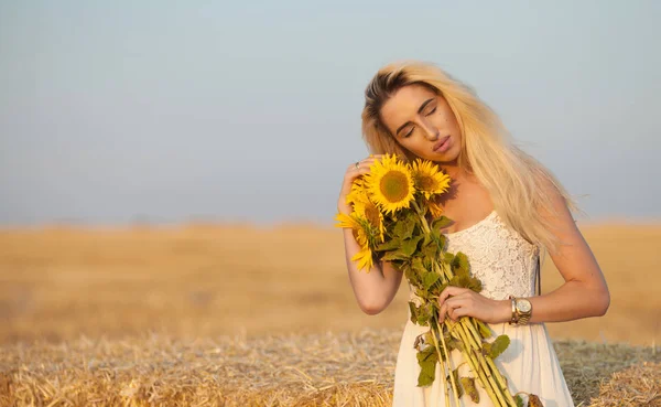 Vacker söt sexig tjej i en vit klänning som går på en fältet solrosor i hand. — Stockfoto