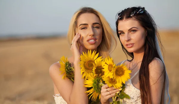 Två flickvänner blondin och brunett i fältet med solrosor i hand. — Stockfoto