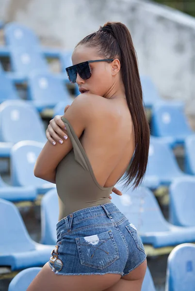 美丽的年轻性感女人穿着牛仔裤短裤在夏季足球体育场 — 图库照片