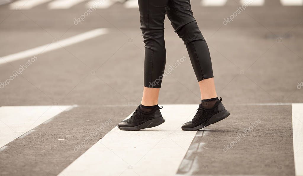 Close up of woman legs walking on crosswalk. The woman is wearing black sneakers.