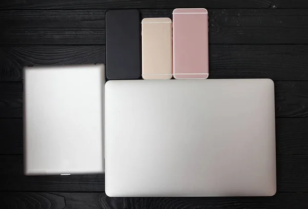 Minimalistic flat lay composition of black & white laptop computer keyboard, cell phone gadget on textured wooden desk table background in bright light. Workspace top view, copy space