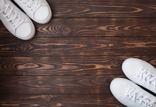 A pair of white canvas shoes on a wooden. White sneakers on brown background.