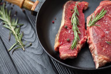 Tuz, baharat ve biberiye bir kızartma tavası ahşap arka plan ile ham taze antrikot biftek