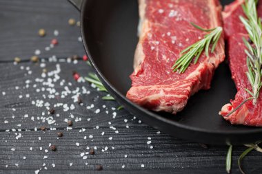 Tuz, baharat ve biberiye bir kızartma tavası ahşap arka plan ile ham taze antrikot biftek