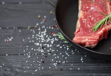 Tuz, baharat ve biberiye bir kızartma tavası ahşap arka plan ile ham taze antrikot biftek