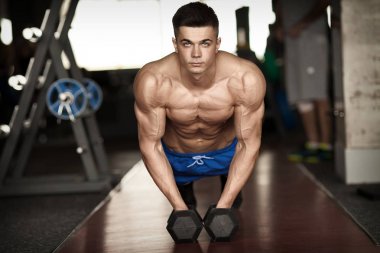 Kaslı vücut geliştirmeci adam spor salonunda dumbbells ile yapıyor