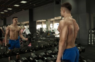 Kaslı vücut geliştirmeci adam spor salonunda dumbbells ile yapıyor