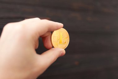 Elini altın litecoin kahverengi bir arka plan üzerinde tutuyor. İş değeri litecoin çok pahalı.