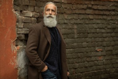 Sakallı yakışıklı, kendine güvenen olgun bir adam mesaj ya da reklam için fotokopi yeri olan paltoda duruyor. Pahalı kıyafetler giymiş, dışarıda poz veren şık zengin bir erkek..