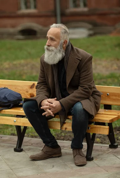 Portrait of a bearded senior man outdoors, sitting on a bench in a park