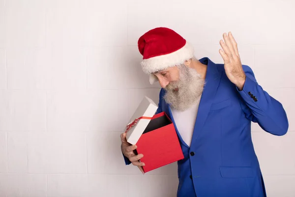 白い背景の上にギフトボックスを持っているハンサムなシニア髭の男とカメラを見て サンタクロースはメリークリスマスと幸せな新年を願っています 青いスーツの男クリスマス — ストック写真