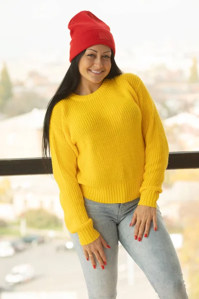 迷人的漂亮姑娘 一头长长的黑发 时尚开朗的年轻女子编织了黄色毛衣 红帽积极向上的真情实感 — 图库照片