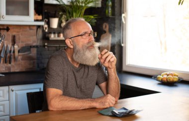 Evde marihuana içen yaşlı sakallı bir adam (esrar, esrar).