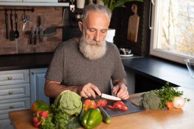 Sakallı yaşlı adam mutfakta sağlıklı ve lezzetli bir salata hazırlıyor..