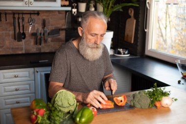 Sakallı yaşlı adam mutfakta sağlıklı ve lezzetli bir salata hazırlıyor..