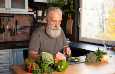 Sakallı yaşlı adam mutfakta sağlıklı ve lezzetli bir salata hazırlıyor..