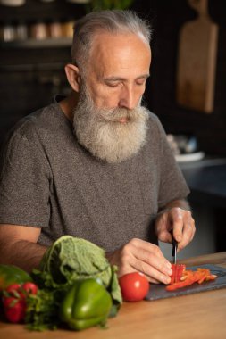 Sakallı yaşlı adam mutfakta sağlıklı ve lezzetli bir salata hazırlıyor..