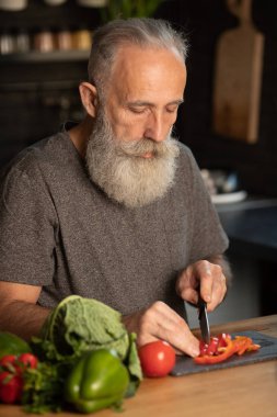 Sakallı yaşlı adam mutfakta sağlıklı ve lezzetli bir salata hazırlıyor..