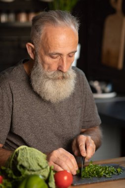 Sakallı yaşlı adam mutfakta sağlıklı ve lezzetli bir salata hazırlıyor..