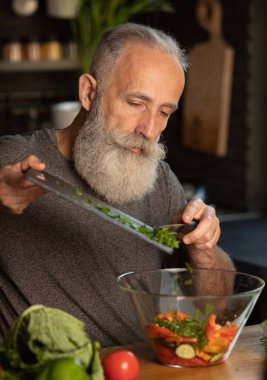 Sakallı yaşlı adam mutfakta sağlıklı ve lezzetli bir salata hazırlıyor..