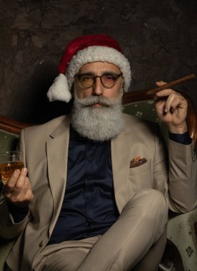 Noel Baba patron brendi içip puro içiyor. Noel Baba şapkalı şık takım elbiseli bir iş adamı. Zengin Xmas kavramı.