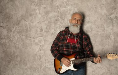 Gri duvara karşı gitarla poz veren şık yaşlı sakallı adam..