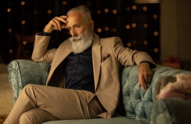 Yetişkin iş adamının son moda takım elbiseli portresi ve ışıklara karşı modern stüdyoda oturması.