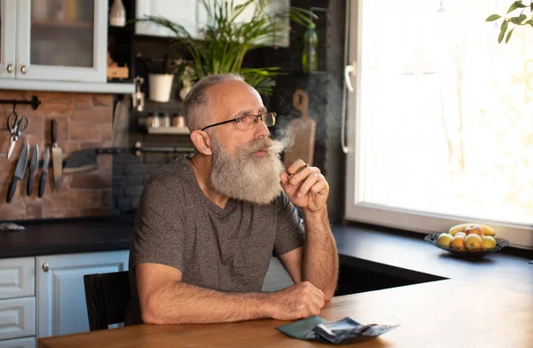 Bearded senior man smoking marijuana (weed, cannabis) at home.
