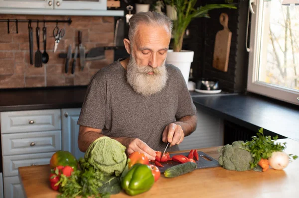 Sakallı yaşlı adam mutfakta sağlıklı ve lezzetli bir salata hazırlıyor..