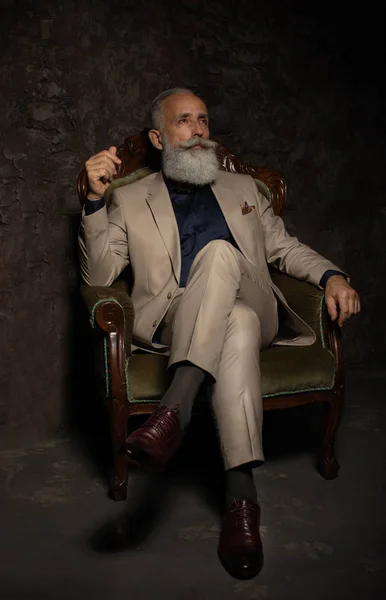 A portrait of a handsome mature man in a formal costume sitting in the armchair in the classic interior. Men\'s beauty, fashion.