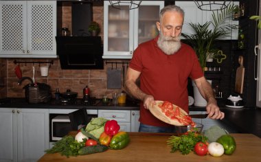 Sakallı yaşlı adam mutfakta sağlıklı ve lezzetli bir salata hazırlıyor..