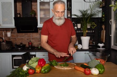 Sakallı yaşlı adam mutfakta sağlıklı ve lezzetli bir salata hazırlıyor..