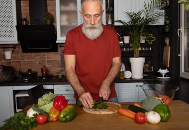 Sakallı yaşlı adam mutfakta sağlıklı ve lezzetli bir salata hazırlıyor..