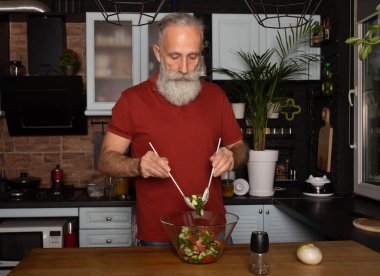 Sakallı yaşlı adam mutfakta sağlıklı ve lezzetli bir salata hazırlıyor..
