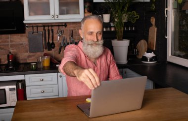 Yapılan işten memnun. Mutlu sakallı kıdemli adam evinde çalışırken dizüstü bilgisayarda çalışıyor..