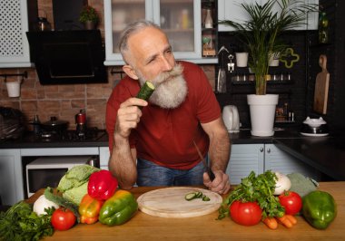 Sakallı kıdemli adam evde yemek pişiriyor mutfakta salata hazırlıyor..