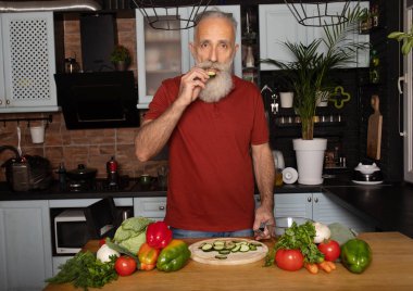 Sakallı kıdemli adam evde yemek pişiriyor mutfakta salata hazırlıyor..