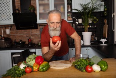 Sakallı kıdemli adam evde yemek pişiriyor mutfakta salata hazırlıyor..