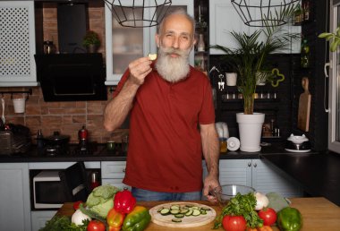 Sakallı kıdemli adam evde yemek pişiriyor mutfakta salata hazırlıyor..