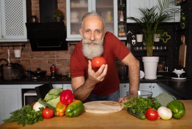 Sakallı kıdemli adam evde yemek pişiriyor mutfakta salata hazırlıyor..