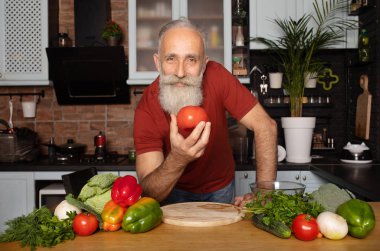 Sakallı kıdemli adam evde yemek pişiriyor mutfakta salata hazırlıyor..