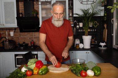 Sakallı kıdemli adam evde yemek pişiriyor mutfakta salata hazırlıyor..