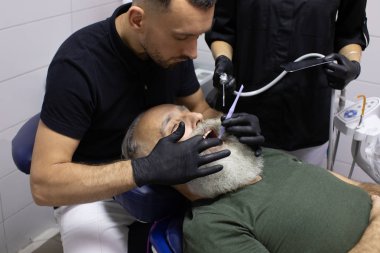 Sakallı yaşlı adam dişçi muayenehanesinde diş tedavisi görüyor..